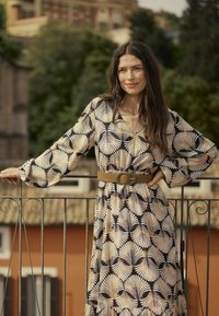 Langärmliges Kleid in Schwarz mit cremefarbenem Blättermuster. Verfügt über einen V-Ausschnitt, geraffte Bündchen und einen braunen Gürtel mit einer Metallschnalle in der Taille.