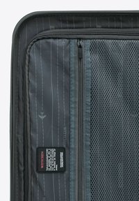 Šedý interiér kufru s síťovanou kapsou, zipovými uzávěry a potištěnými liniemi. Obsahuje černou visačku s bílým textem. Odolná tkanina.