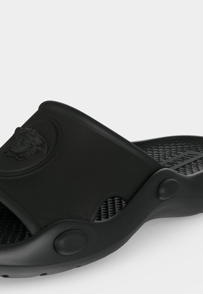 Sandale slide en caoutchouc noir avec une semelle intérieure texturée et un logo tête de Méduse embossé sur la large bride.