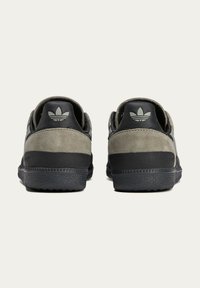 Grey suede and black leather sneakers feature a textured heel, rubber sole, and embossed logo on the back. Minimalist design with tonal accents.