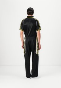 Black athletic tracksuit made of smooth fabric, featuring yellow and white accents, side patterns, and a relaxed fit with an elastic waistband.