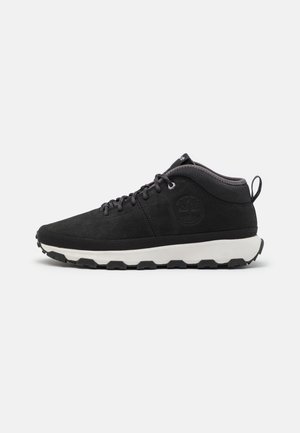 Sneaker de ante negro de caña media con suela blanca acolchada, diseño de cordones y un logotipo en el costado. Acentos texturizados alrededor del tobillo.