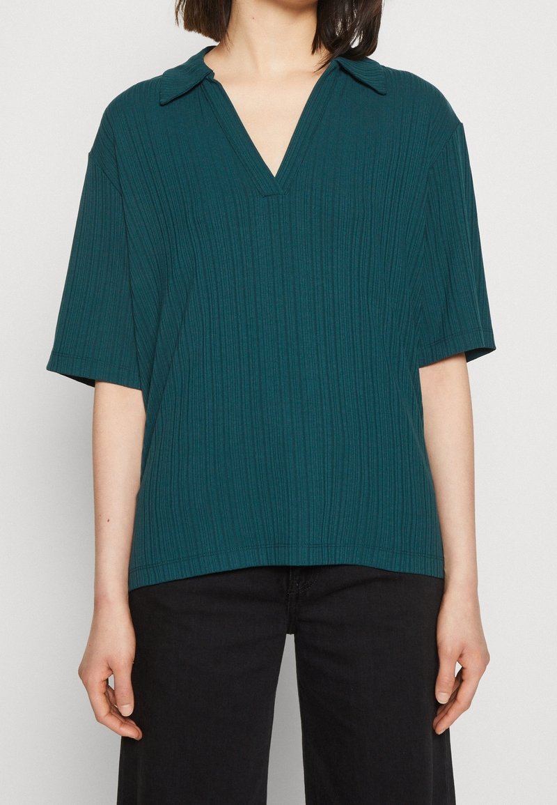 Teal ribbad kortärmad blus med V-ringning och spetsig krage. Tyget har en texturerad yta med vertikala linjer och en avslappnad passform.