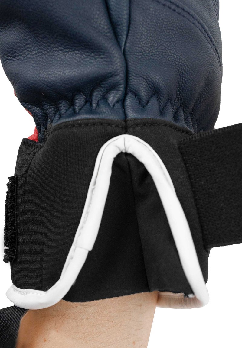 Läderhandske i marinblå färg, med elastisk mudd, svart textilband och vit kant. Har samlad sömnad vid handleden.