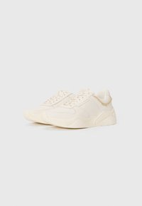 White sneakers with a textured finish, featuring a chunky sole, lace-up design, and a subtle decorative chain on the heel.