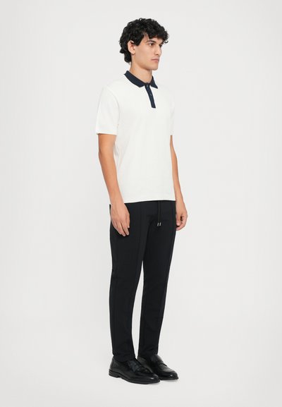 Hvit polo skjorte med marineblå krage, svarte skreddersydde bukser og svarte sko. Enkel design, glatt tekstur og tilpasset form.