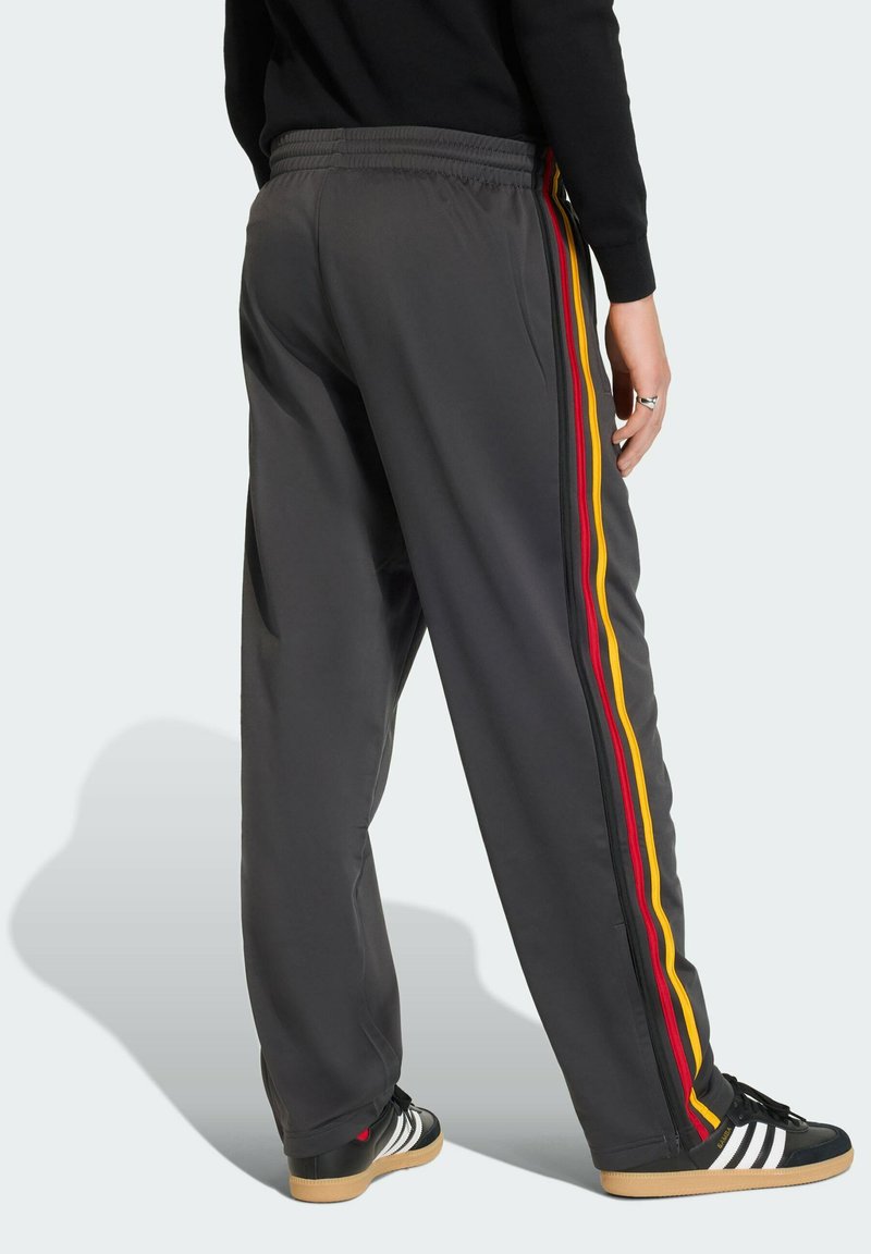 Gray athletic pants feature yellow, red, and black side stripes. The fabric has a smooth texture with an elastic waistband for a comfortable fit.