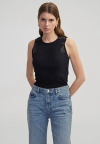 Top sin mangas negro con detalle de encaje en los hombros, combinado con jeans de tiro alto en azul claro. Presenta un escote redondo y un ajuste slim.