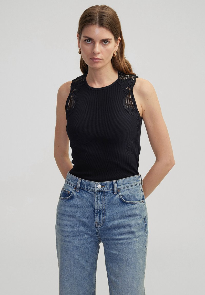 Top sin mangas negro con detalle de encaje en los hombros, combinado con jeans de tiro alto en azul claro. Presenta un escote redondo y un ajuste slim.