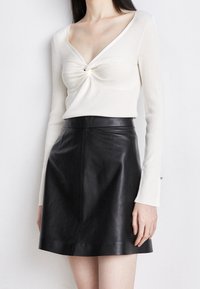 Top a maniche lunghe a coste crema con un davanti annodato; abbinato a una mini gonna in pelle nera, texture liscia, design aderente.