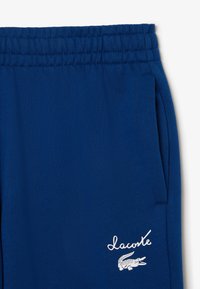 Blaue Baumwoll-Jogginghosen mit elastischem Bund, seitlichen Taschen und einem weißen Lacoste-Logo mit Krokodil-Detail.