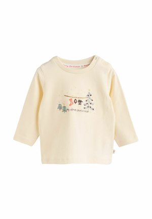 Long-sleeve cream cotton shirt featuring a festive illustration with a tree, stocking, and text "my first Christmas." Snap button on shoulder.