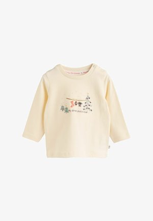 Camicia a maniche lunghe in cotone crema con un'illustrazione festiva che raffigura un albero, una calza e la scritta "il mio primo Natale". Pulsante a pressione sulla spalla.