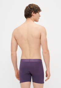 Boxers em algodão roxos para homem com um ajuste justo, apresentando uma cintura suave e uma marcação mínima na parte de trás. Design simples, sem padrões.