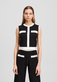 Black cropped top with white textured panels and a round neckline, paired with black wide-leg pants featuring white accents and a patterned texture.