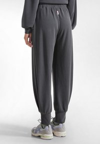 Graue Jogginghosen aus weichem Material, mit einem elastischen Bund, gerippten Knöcheln und einem kleinen Etikett auf der Rückseite.