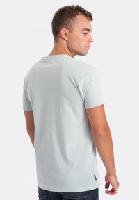 T-shirt grigio chiaro a maniche corte con scollo rotondo, texture liscia e spacchi laterali all'orlo. La vista posteriore mostra un design semplice.