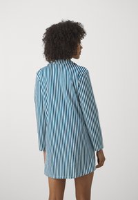 Zila un baltā striped krekla kleita ar apkakli, garām piedurknēm un pārāk lielu piegriezumu. Audums šķiet gluds ar vieglu spīdumu.