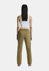 Khaki-Hosen mit entspannter Passform, elastischem Bund und dezentem Logodetail. Kombination mit einem weißen, kurzen Tanktop, das eine glatte Textur aufweist.