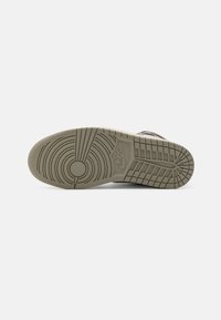 Semelle d'une chaussure Nike grise montrant des motifs de bande de roulement circulaires et rectangulaires avec le logo Nike dans la partie centrale.