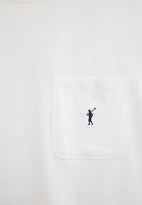 Tissu blanc avec une poche carrée cousue ornée d'une petite silhouette bleu marine d'une personne tenant un outil sur l'épaule.