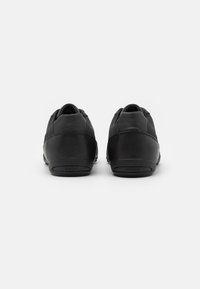 Black leather sneakers featuring a smooth texture and rounded design, with a low profile and discreet logo on the heel.