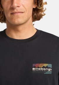 Black cotton t-shirt featuring a multicolored graphic logo on the left chest area depicting mountains and the text "Billabong Adventure Division."
