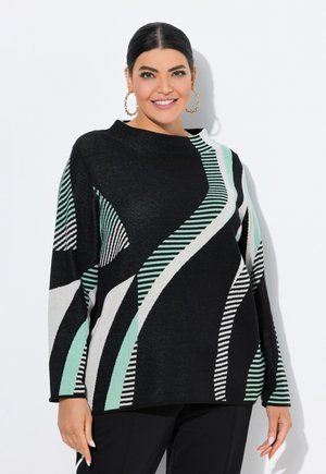 Femme aux cheveux noirs en chignon bas, portant de grandes boucles d'oreilles en or et un pull noir avec des motifs abstraits en rayures blanches et menthes.