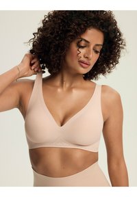 Nude bezprzewodowy stanik z dekoltem w kształcie litery V, szerokimi ramiączkami i kropkowymi akcentami wzdłuż pasa. Gładka tekstura, lekki materiał.