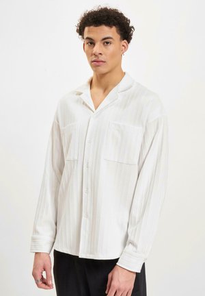 Witte button-up overhemd met verticale strepen, lange mouwen, twee borstzakken en een ontspannen kraag. Zachte, gladde stof met een subtiele textuur.