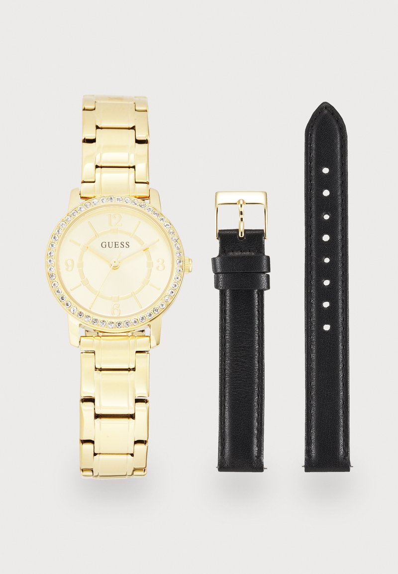 Arany színű óra kerek számlappal, ezüst részletekkel és kristályokkal díszített tokkerettel; levehető fekete bőrszíjjal rendelkezik.