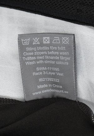 Sort tre-lags vest med en glat grå indvendig foring, med plejeinstruktioner trykt på et stofmærke, sikkert syede kanter.