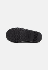 Semelle de chaussure en caoutchouc noir avec un motif de bande de roulement en zigzag, présentant une surface texturée et un détail de marque, offrant traction et durabilité.
