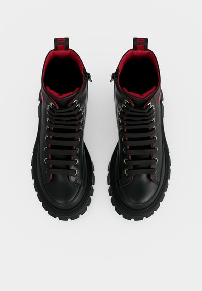 Paire de baskets montantes en cuir noir avec semelles épaisses, lacets noirs, doublure intérieure rouge et languettes au talon.