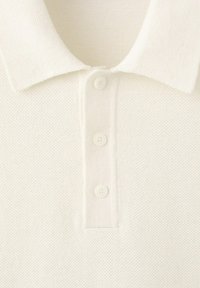 Bílý texturovaný límec polo trička se třemi přišitými knoflíky na légě, zobrazující detaily pletené látky.