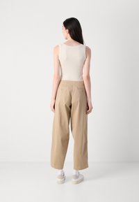 Beige mouwloos topje in combinatie met lichtbruine wijde broek. De broek heeft achterzakken en een relaxte pasvorm. Witte en beige schoenen maken de look compleet.