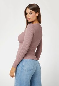Top a maniche lunghe a costine in malva con una silhouette aderente, abbinato a jeans a gamba larga di colore blu chiaro. Presenta un collo rotondo e maniche strutturate.