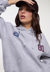 Felpa grigia in cotone con scollo a V, caratterizzata da una toppa blu con la scritta "Colorado" e un grande numero "80" color granata sul davanti, completa di coulisse.