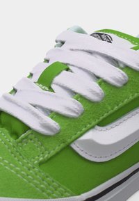 Πράσινο και άσπρο αθλητικό παπούτσι Vans με χοντρές άσπρες κορδόνια δεμένα, υφές σουέντ και καμβά, και ορατό λογότυπο Vans στη γλώσσα.