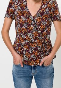 Top floral con mangas cortas, con una base color burdeos oscuro y flores multicolores en naranja, blanco y verde. Diseño peplum.