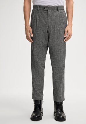 Pantaloni grigi con texture e motivo a quadri, con pieghe davanti e chiusura a bottone. Indossati con stivali neri stringati.