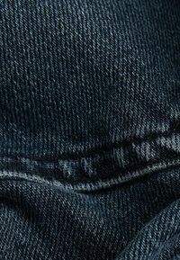 Tissu en denim bleu foncé avec un motif de tissage visible, présentant une texture lisse et des coutures contrastantes le long des coutures, partiellement plié.