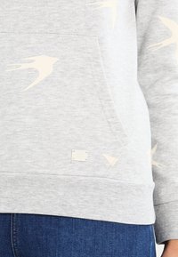 Sudadera gris hecha de una mezcla de algodón, con estampados de golondrinas crema, un bolsillo frontal y una pequeña etiqueta en el dobladillo. Puños y dobladillo acanalados.