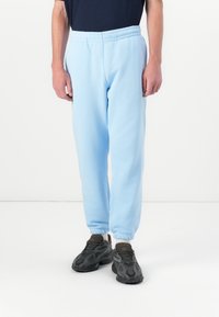 Lyseblå joggebukser laget av mykt stoff, med elastisk midje og mansjetter. Brukt med mørke, uformelle sneakers.
