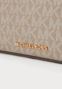 Borsa beige con motivo a monogramma, superficie testurizzata e accento in metallo dorato con logo. I bordi sono rinforzati con rifiniture marroni.