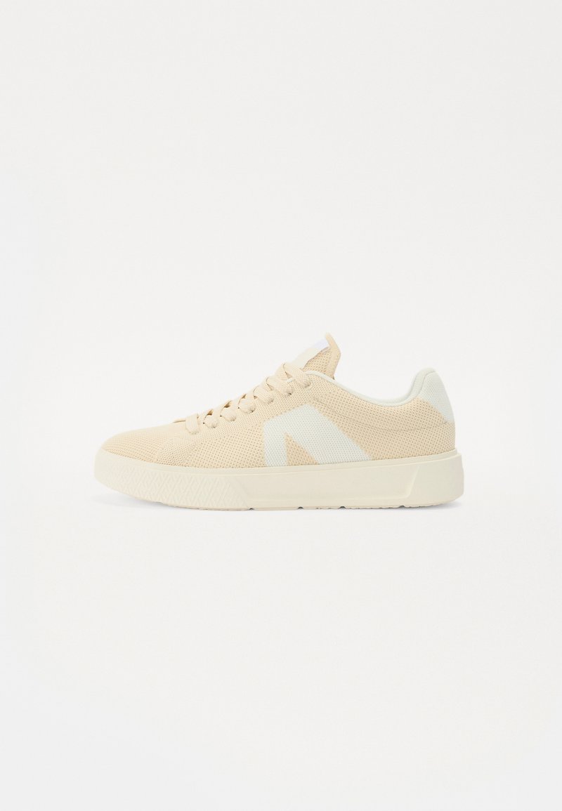 Beige mesh sneakers with a white logo accent. Rounded toe, lace-up design, textured rubber sole, and padded collar for comfort.