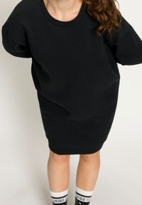 Robe-sweat noire oversize à manches courtes, avec un col côtelé et un design uni. Associée à des chaussettes blanches avec un texte noir.