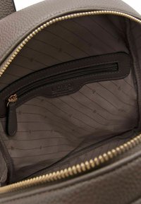 Interno di uno zaino in pelle marrone texture con cerniera dorata, dotato di una tasca separata con cerniera e un sottile motivo a righe.