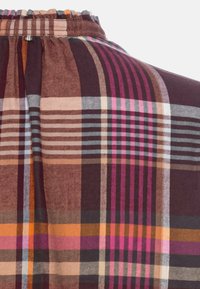 Gros plan sur une ceinture élastique en tissu écossais marron, orange et rose avec des rayures verticales et horizontales et des coutures froncées.