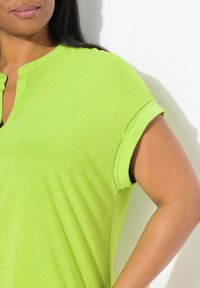 Top verde lime a maniche corte con scollo a V e maniche arrotolate, realizzato in un morbido tessuto testurizzato. Design semplice e pulito senza motivi.